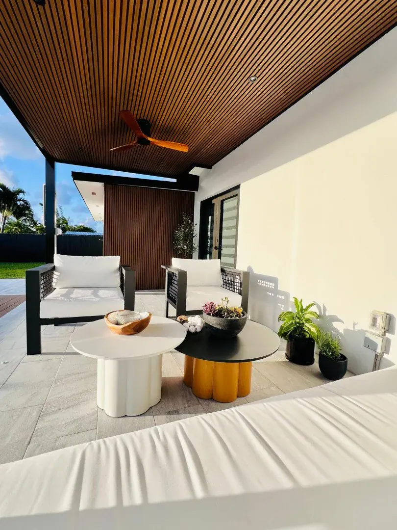 Covered patio seating area under a slatted timber ceiling, with a ceiling fan and low round tables